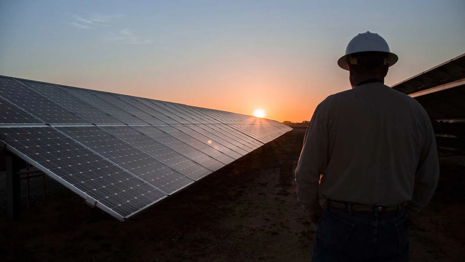 Solar panels at sunrise at the CoServ Solar Station in Krugerville, Texas, with a worker overlooking the rural energy infrastructure
